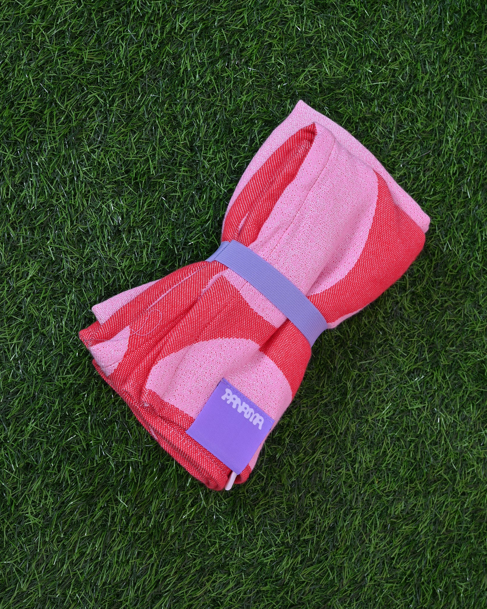 Różowo-czerwony ręcznik plażowy MALINA, zwinięty i związany fioletowa gumą