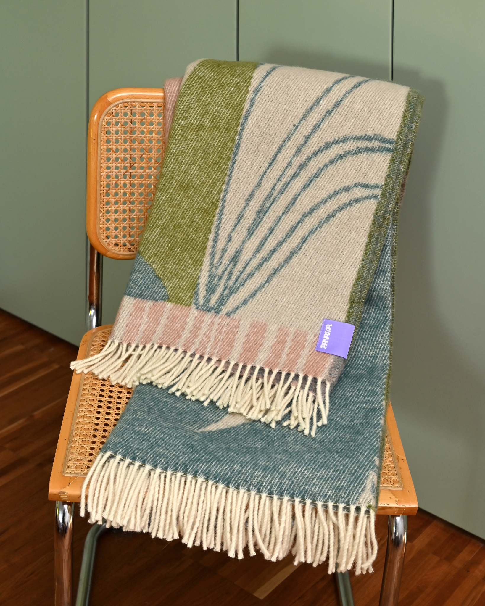 Wełniany koc żakardowy GAJA, odcienie zieleni, beżu i różu, złożony na krześle