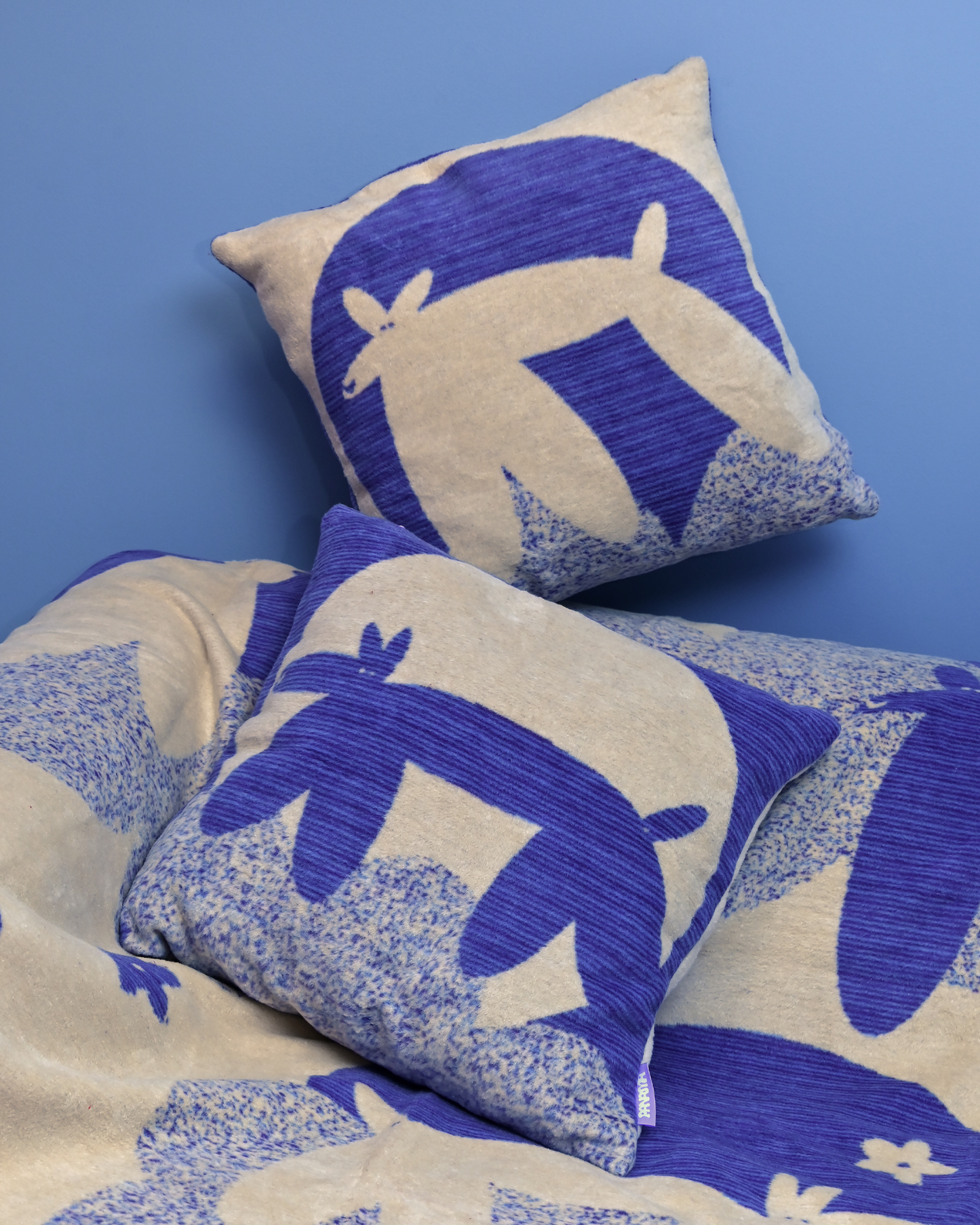 Dwie żakardowe poszewki Niebiańskie pieski na kocu z tej serii, na tle niebieskiej ściany